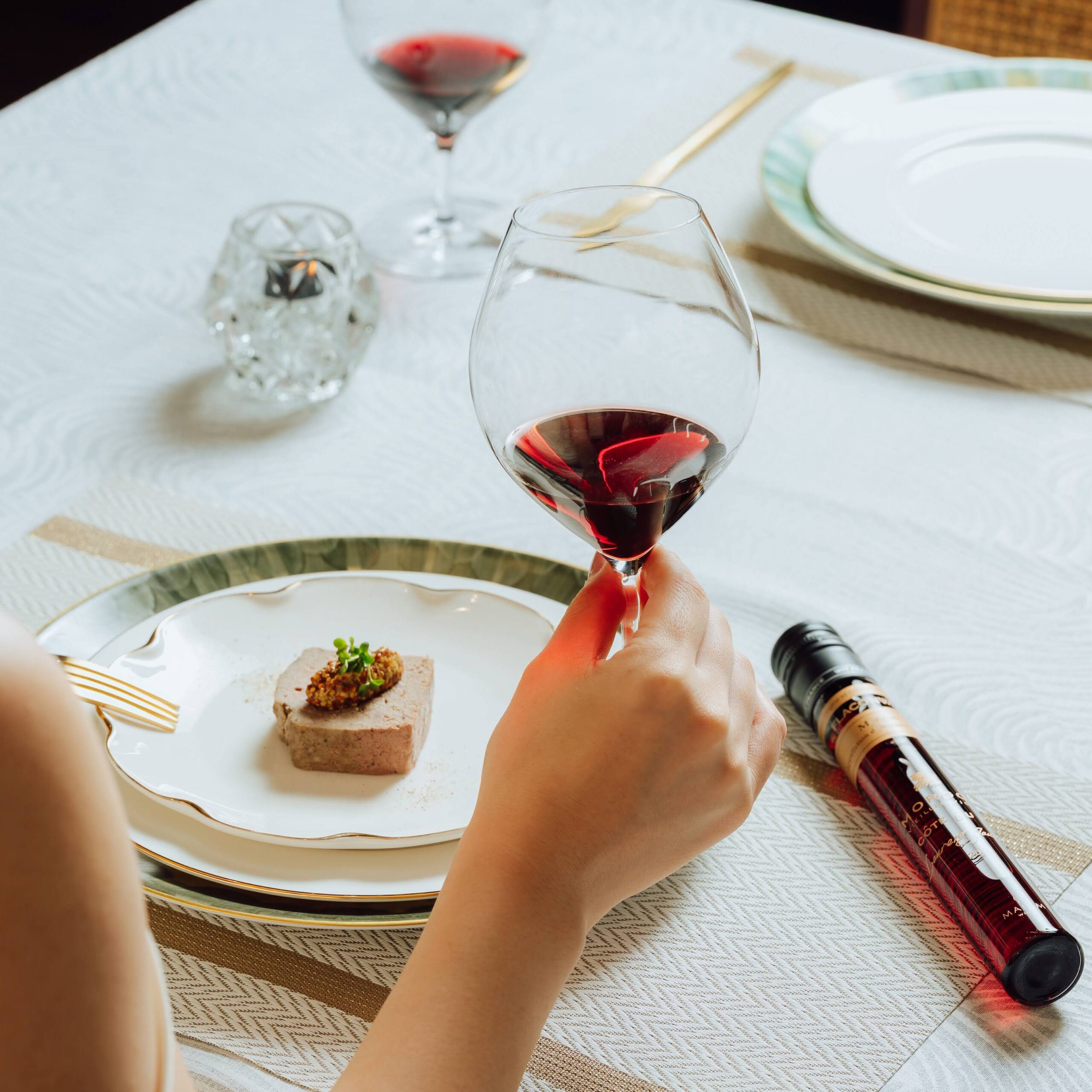 ワイングラスのステムを持つ手元と料理